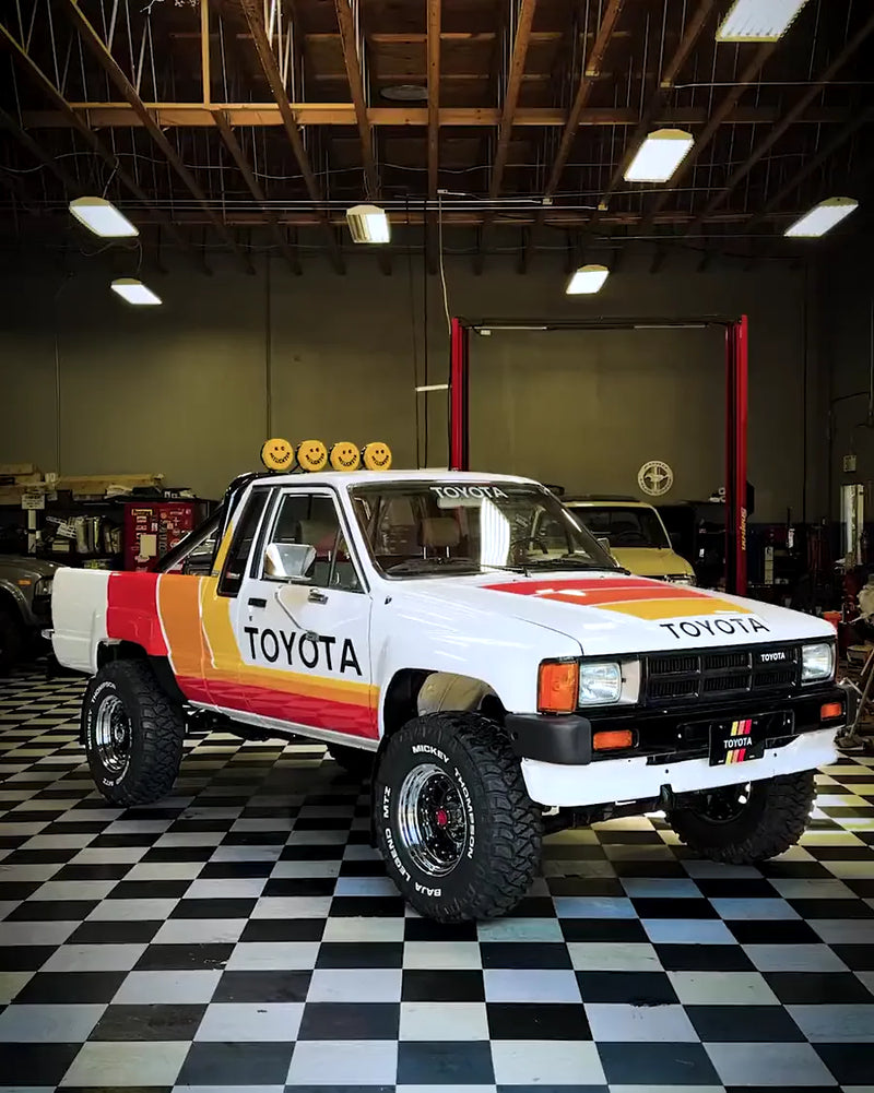 Front view of the white Toyota in a garage with yellow smiley-face covers on the roll-bar lights