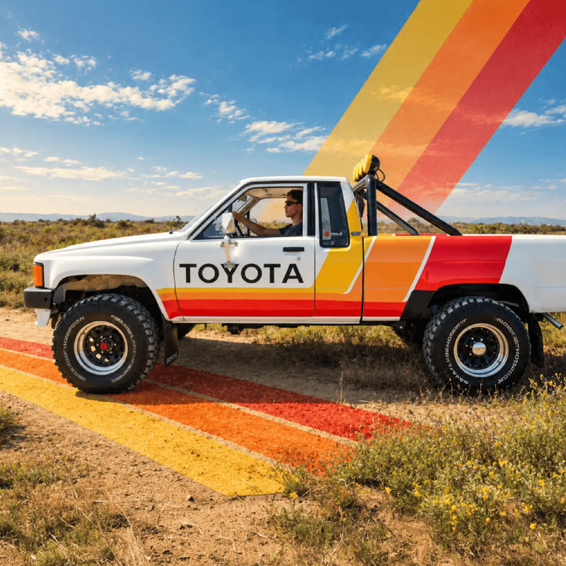 Profile of the white Toyota on a dirt track with stripes running along the bed and door