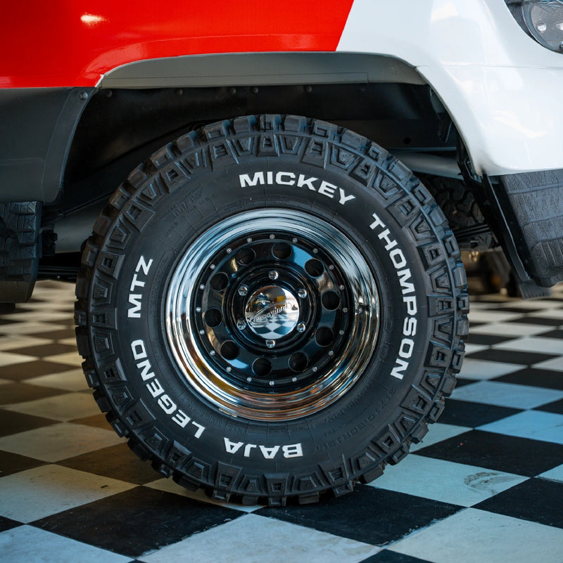 A Mickey Thompson tire mounted on a black-and-chrome wheel beneath a red and white fender